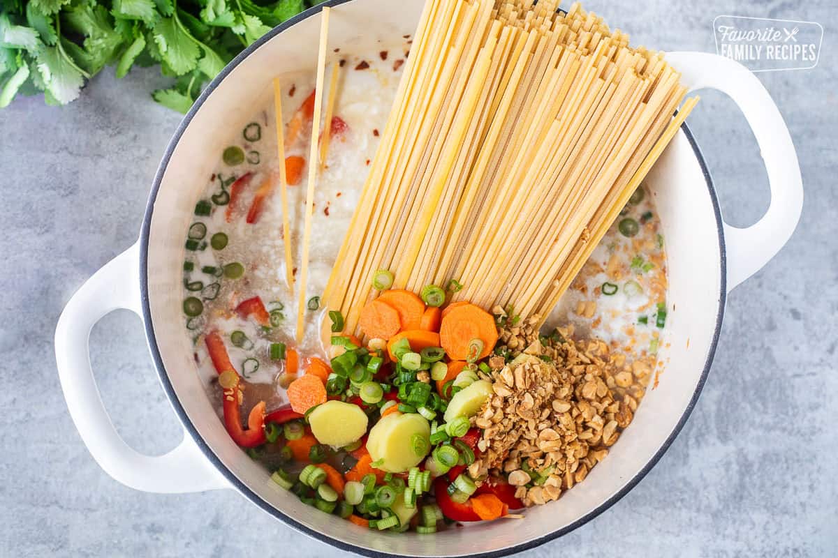 Pot with linguine, chicken broth, fish sauce, soy sauce, peanuts, coconut milk, carrot, green onion, red bell pepper, ginger, peanut butter, brown sugar, and garlic.
