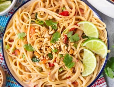 Plate of Thai Peanut Noodles with lime wedges, cilantro, and peanuts.