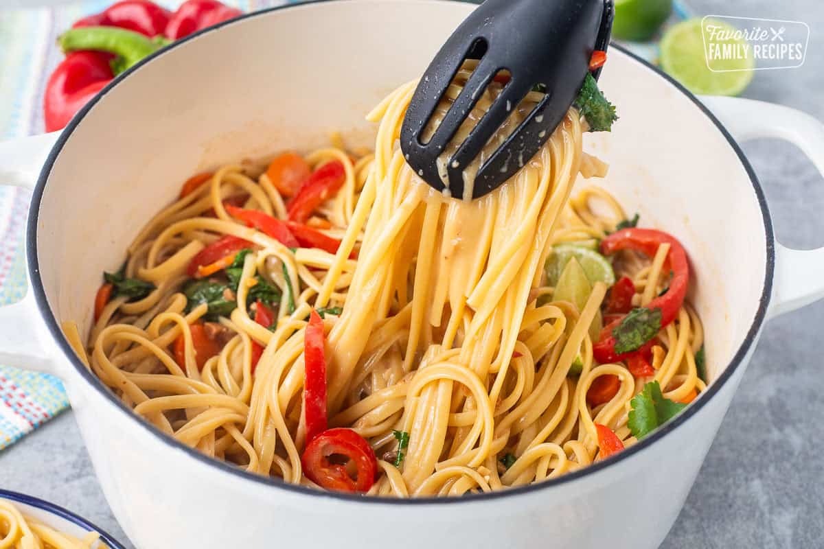 Pulling up Thai peanut noodles with tongs from pot.
