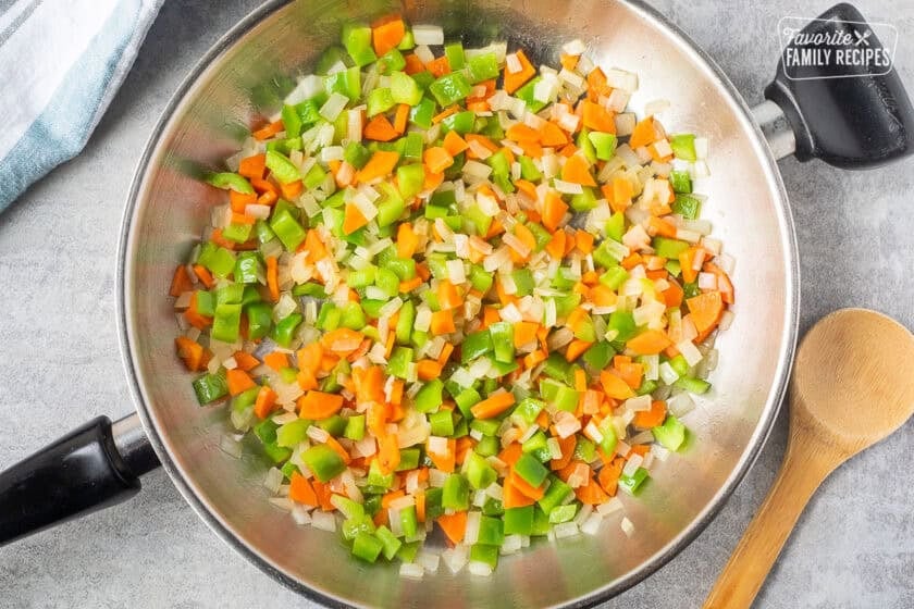 Skillet with cooked green bell pepper, carrot and white onion.
