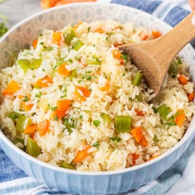 Wooden spoon in Bowl of Vegetable rice with green peppers, carrot and onion. Garnished with fresh parsley.