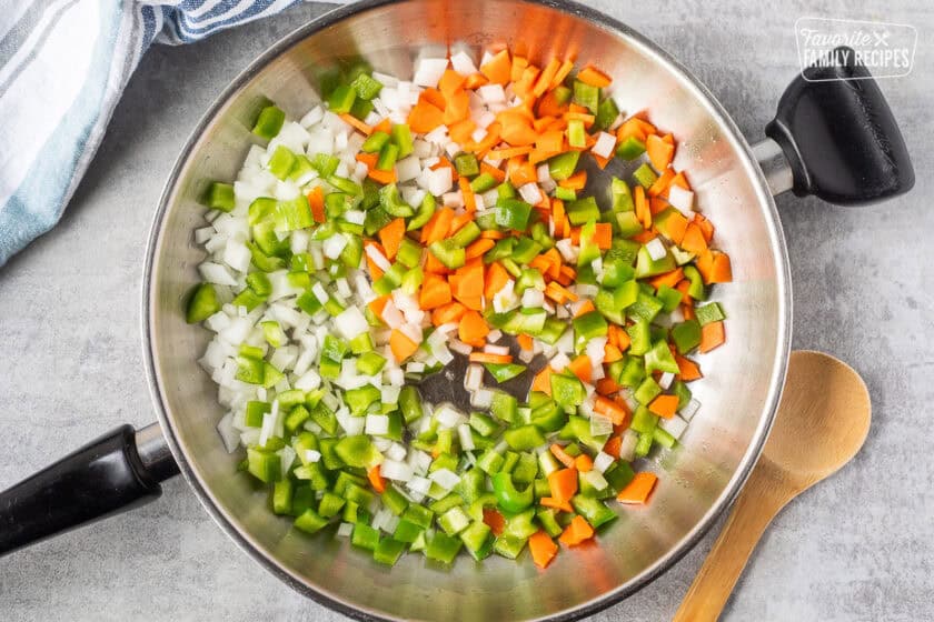 Skillet with cut green bell pepper, carrot and white onion.