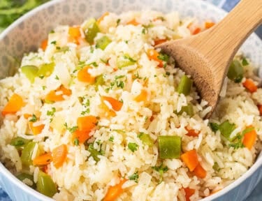 Wooden spoon in Bowl of Vegetable rice with green peppers, carrot and onion. Garnished with fresh parsley.