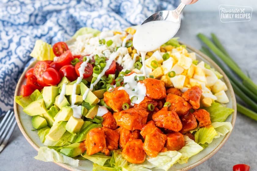Pouring Ranch on top of buffalo chicken salad.
