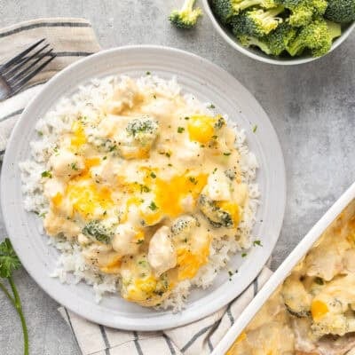 Plate of chicken divan over rice next to casserole dish and bowl of rice and bowl of broccoli.