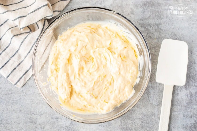 Glass mixing bowl with cream of chicken and cheese mixture. Spatula on the side.