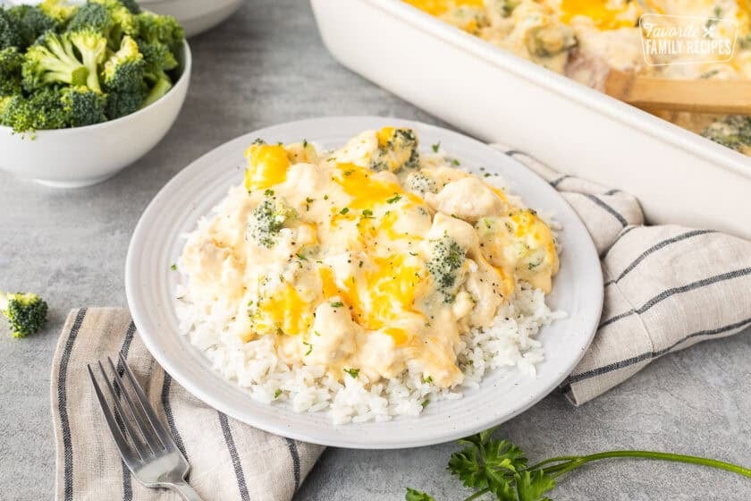Plate of chicken divan over rice next to casserole dish and bowl of rice and bowl of broccoli.