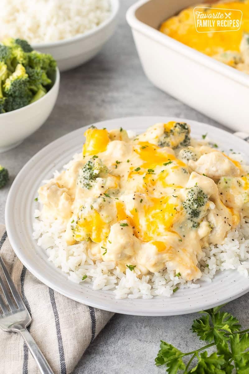 Plate of chicken divan over rice next to casserole dish and bowl of rice and bowl of broccoli.
