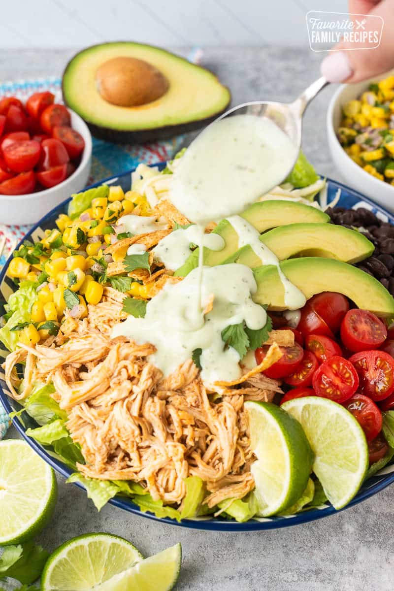 Drizzling cilantro ranch dressing on top of a southwest chicken salad.