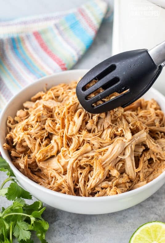 Bowl of Crockpot Mexican Shredded Chicken with tongs.