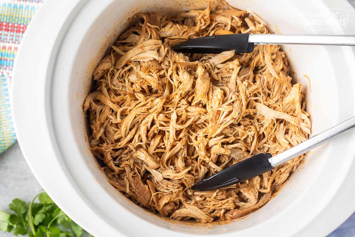 Mexican Shredded Chicken in the crockpot with tongs.