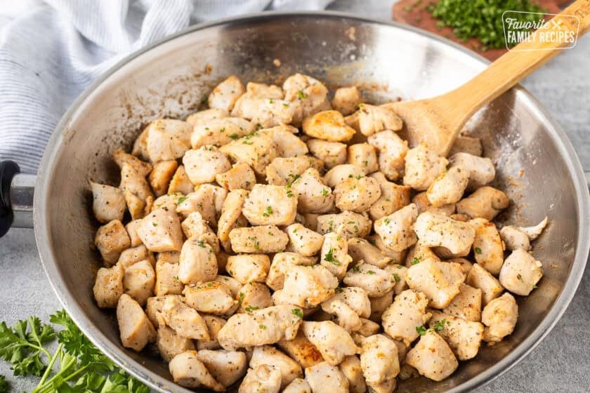 Skillet of diced chicken and wooden spoon.