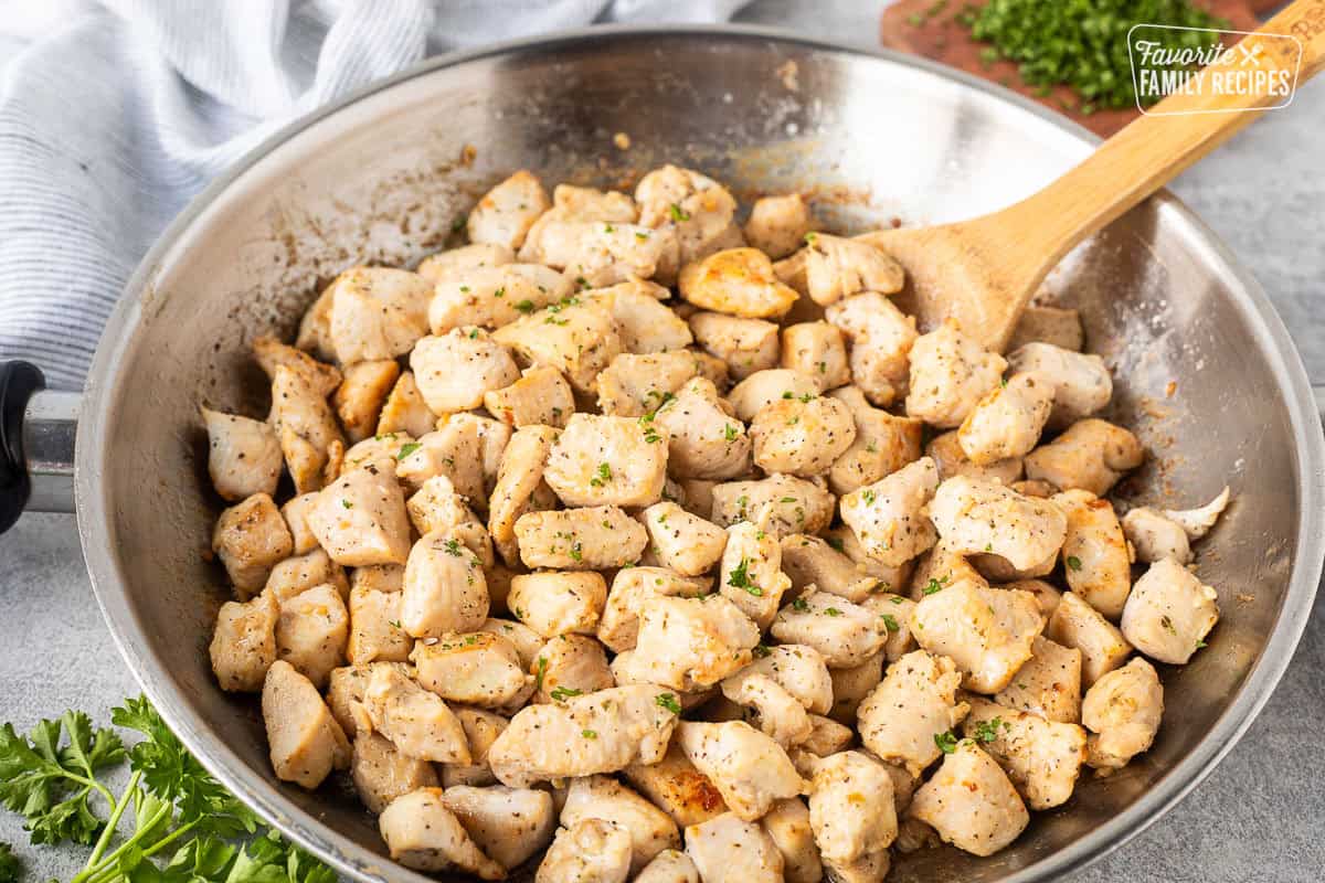 Skillet of diced chicken and wooden spoon.