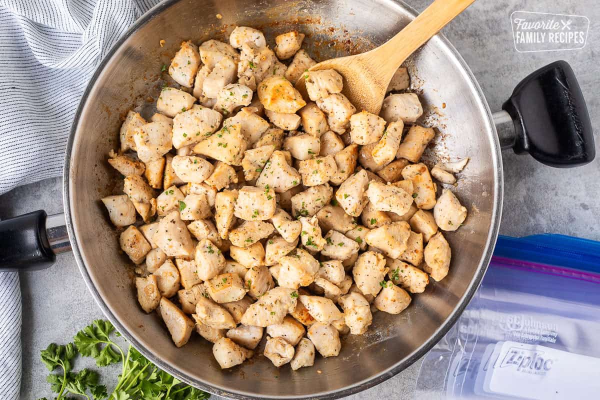 Skillet of diced chicken and wooden spoon. Ziplock bags on the side.
