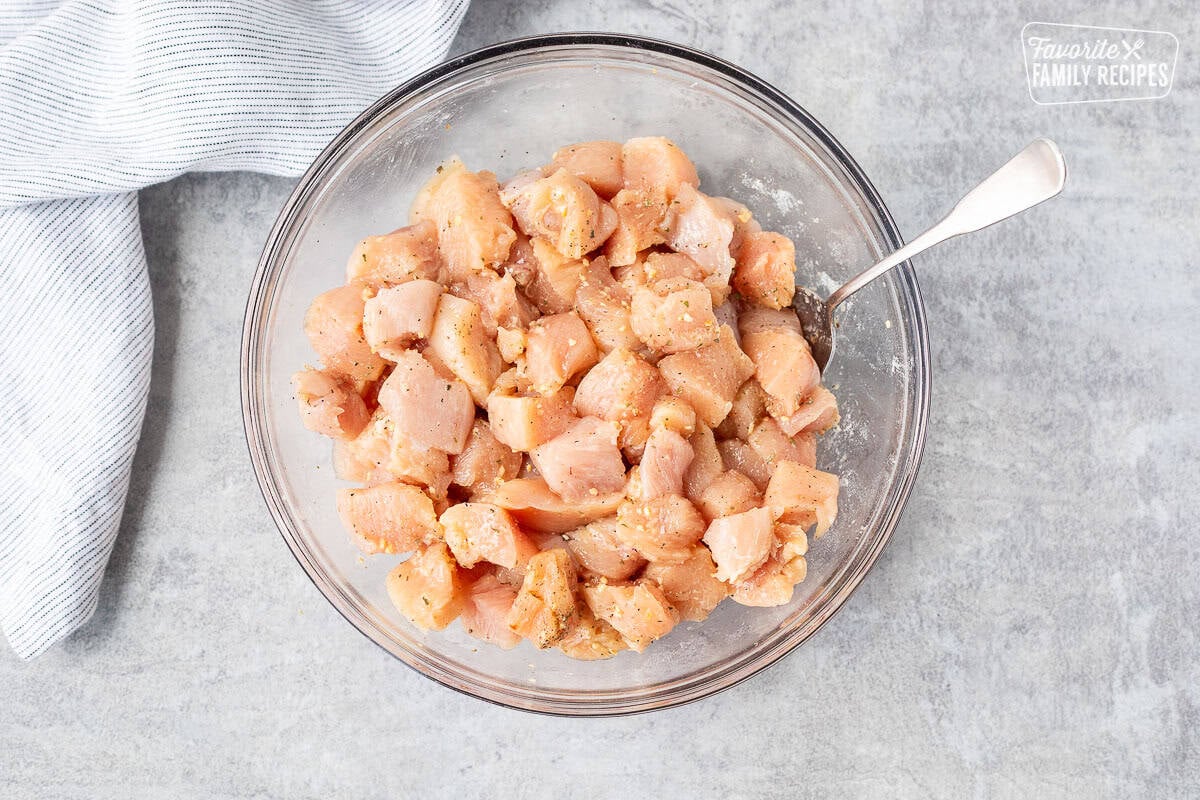 Glass bowl with diced chicken mixed with seasonings and a spoon.