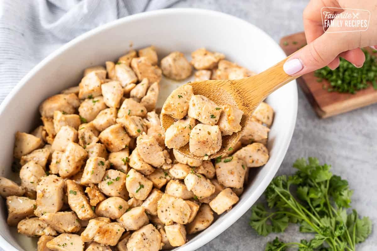 Holding diced chicken on a wooden spoon over casserole dish.