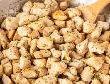 Skillet of diced chicken and wooden spoon.