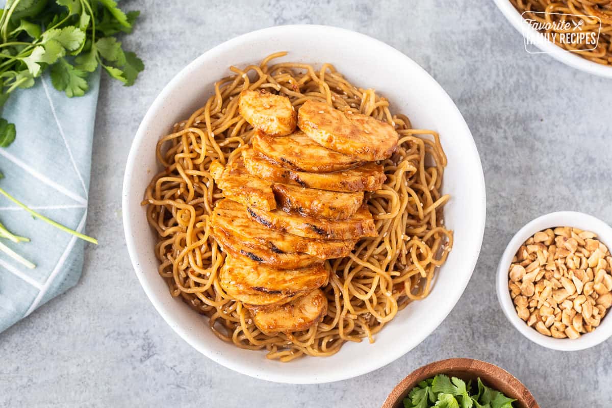 Peanut chicken topped on sweet and spicy noodles in a bowl.
