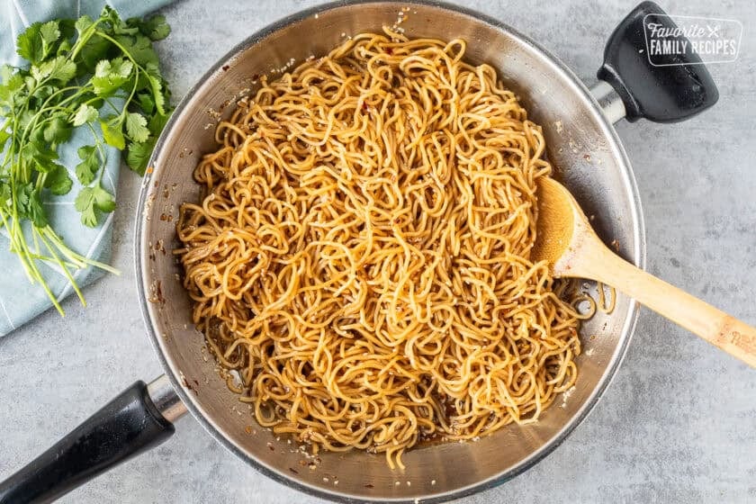 Mixing noodles with sweet and spicy sauce in a skillet.