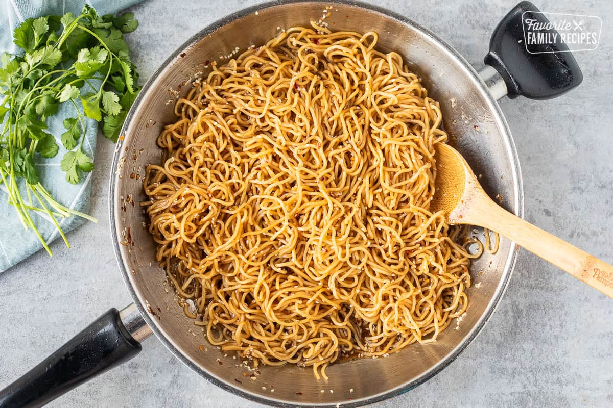 Mixing noodles with sweet and spicy sauce in a skillet.