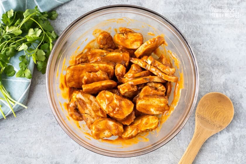 Glass bowl with grilled chicken strips marinating in peanut sauce.