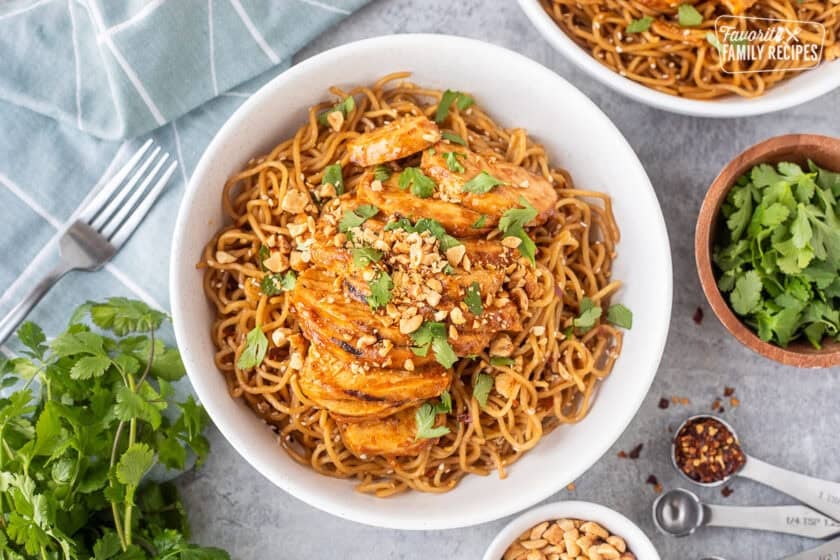 Sweet and spicy noodles with grilled chicken in a bowl and topped with cilantro and peanuts.