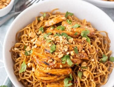 Sweet and spicy noodles with grilled chicken in a bowl and topped with cilantro and peanuts.
