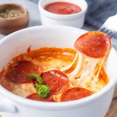Lifting a pepperoni from cottage cheese pizza bowl with the cheese pulling.