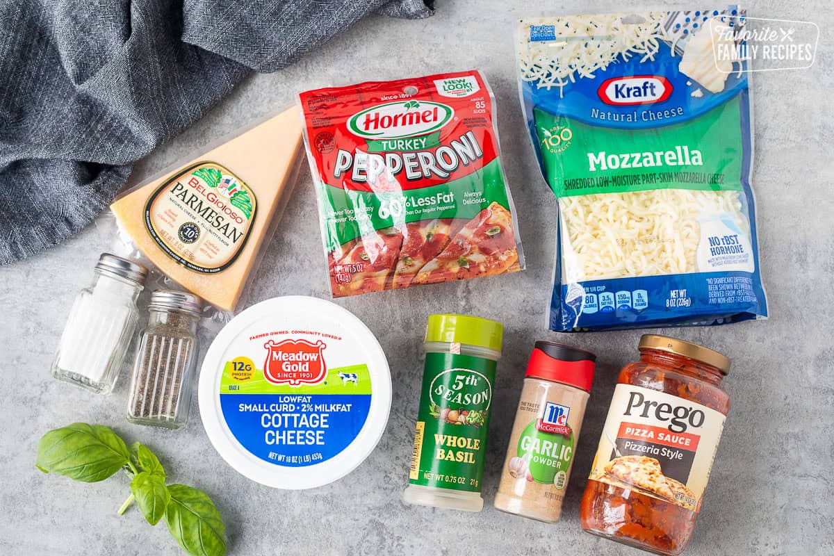Ingredients to make cottage cheese pizza bowl including parmesan cheese, turkey pepperoni, mozzarella cheese, cottage cheese, basil, garlic powder, pizza sauce, salt, pepper and fresh basil.