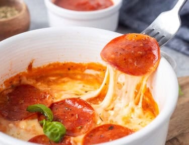 Lifting a pepperoni from cottage cheese pizza bowl with the cheese pulling.