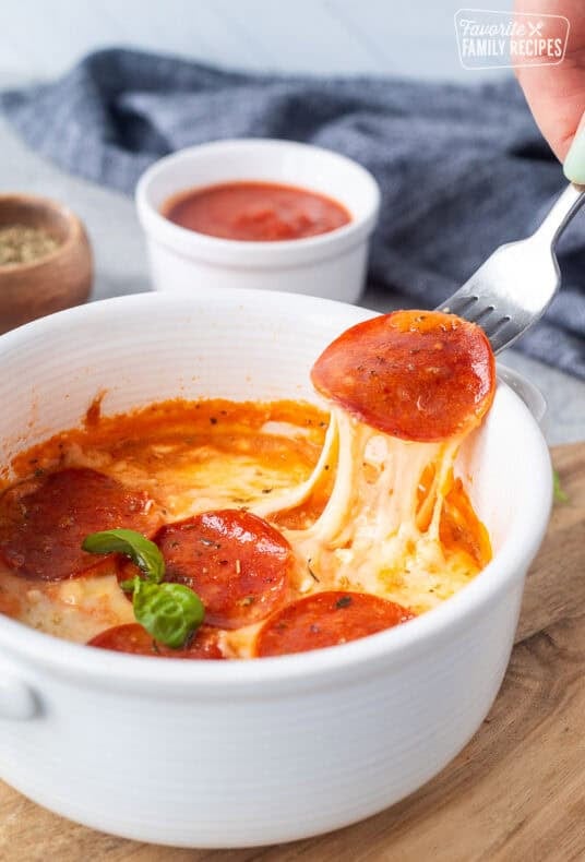 Lifting a pepperoni from cottage cheese pizza bowl with the cheese pulling.