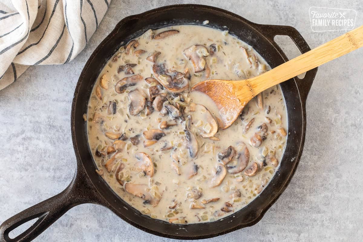 Milk added to mushroom and onion roux in a skillet and stirred with a wooden spoon.