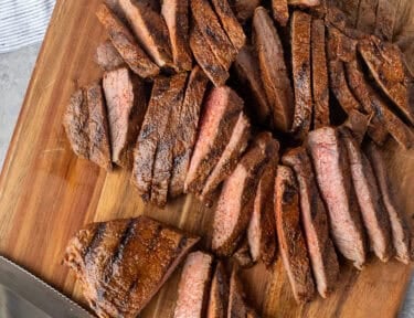 Sliced steak on a cutting board with a knife.