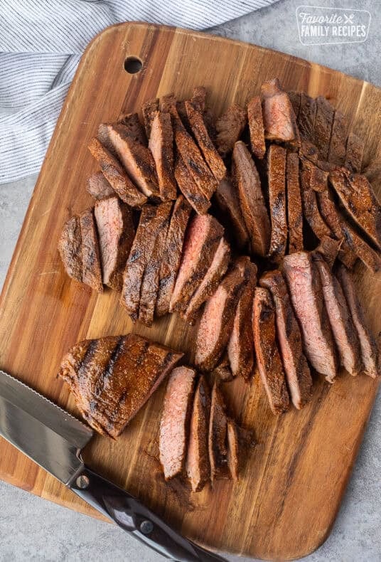 Sliced steak on a cutting board with a knife.