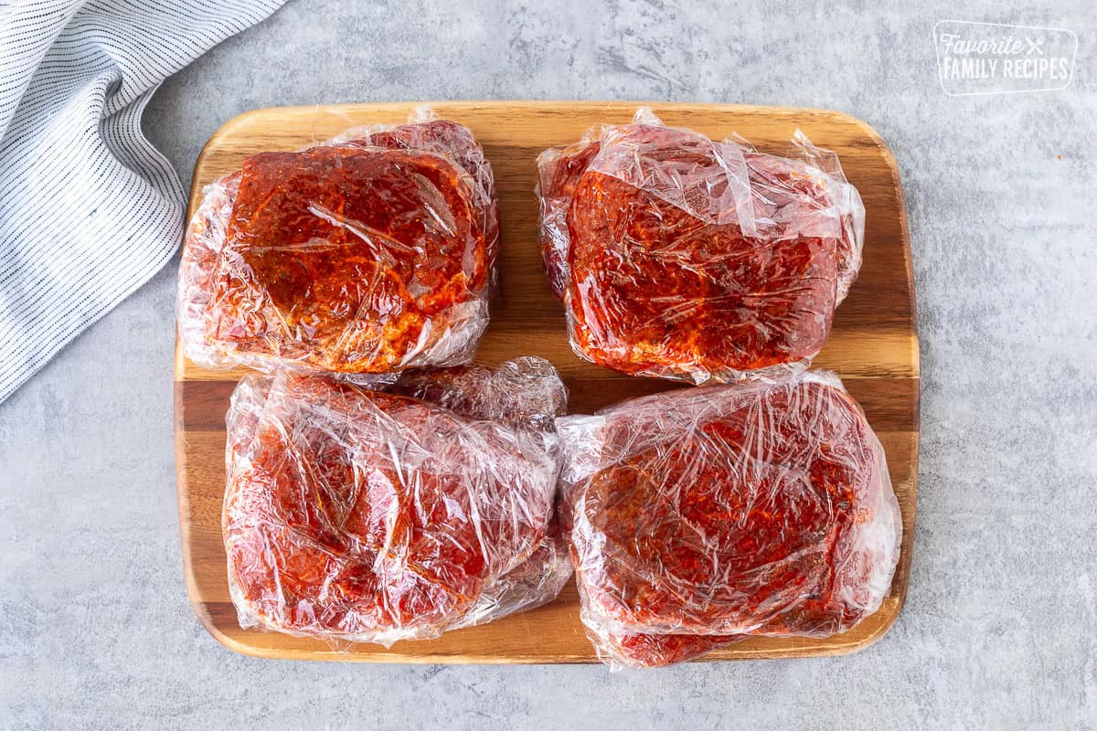 Seasoned steaks wrapped with plastic wrap.