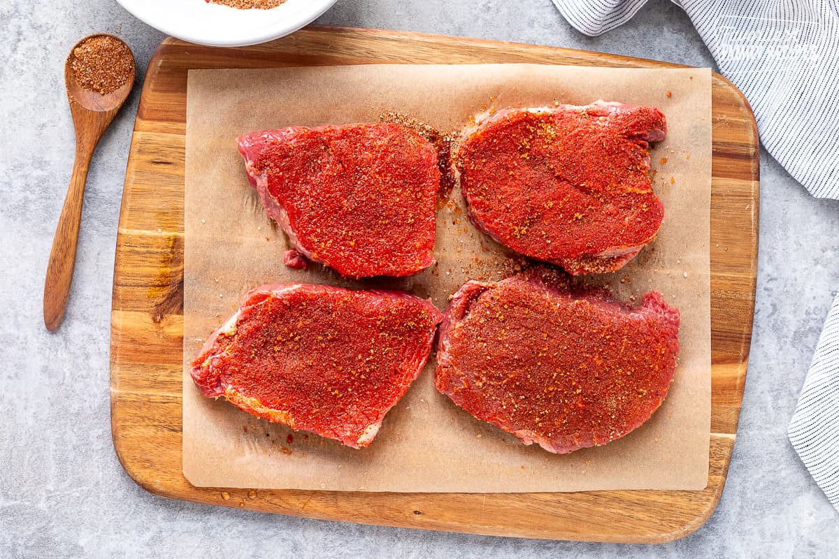 Seasoned steaks on a parchment lined cutting board.