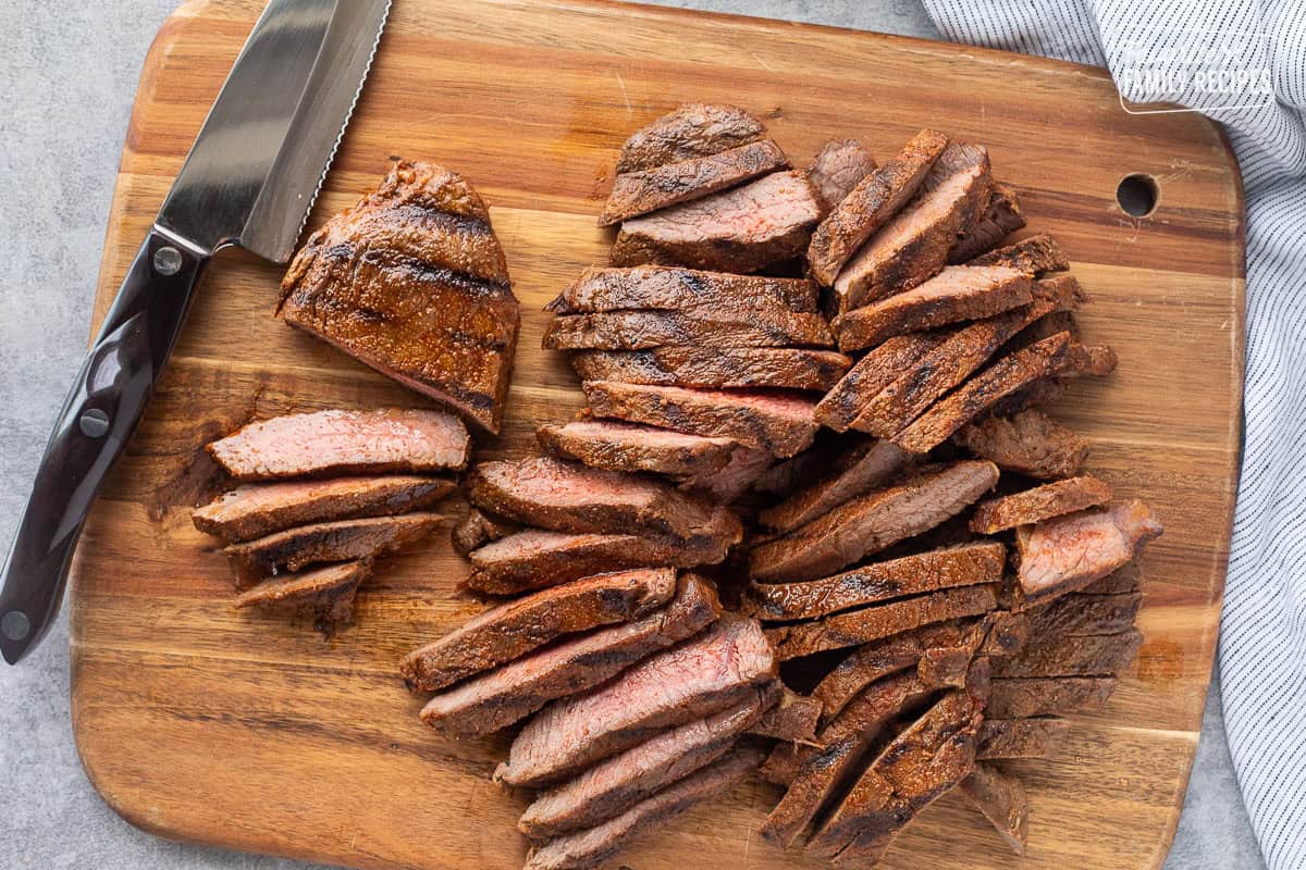 Slicing grilled steaks on a cutting board.