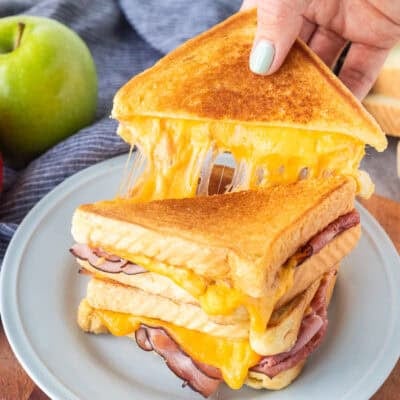 Pulling a half of grilled ham and cheese with the melted cheese pulling from the other half of the sandwich.