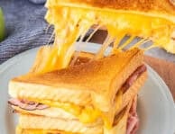 Pulling a half of grilled ham and cheese with the melted cheese pulling from the other half of the sandwich.