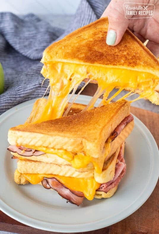 Pulling a half of grilled ham and cheese with the melted cheese pulling from the other half of the sandwich.