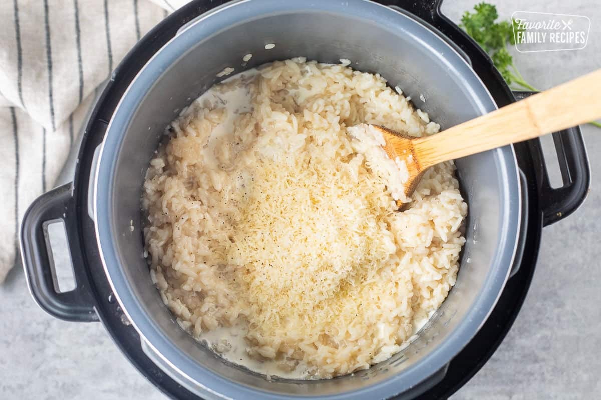 Stirring in parmesan cheese, cream, salt and pepper into risotto with wooden spoon.