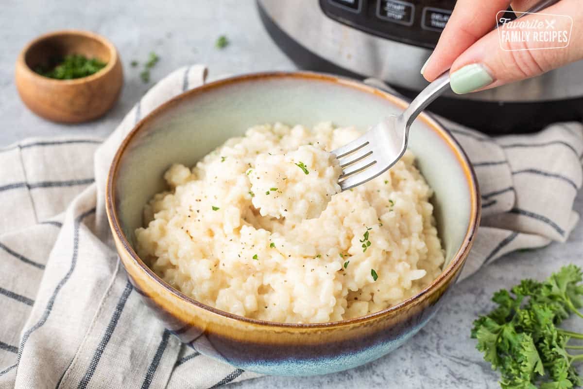 Fork lifting up a bite of instant pot risotto from a bowl.