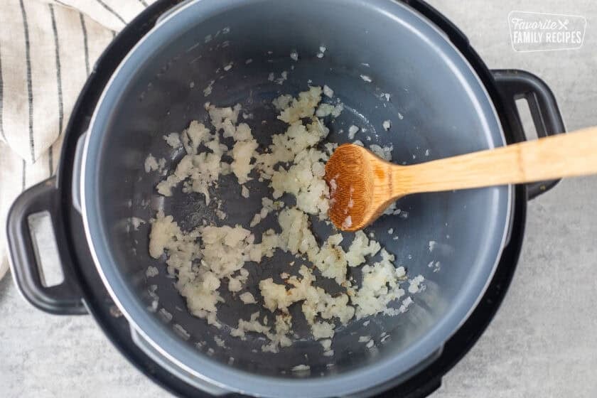 Instant pot with sautéed onions and wooden spoon.