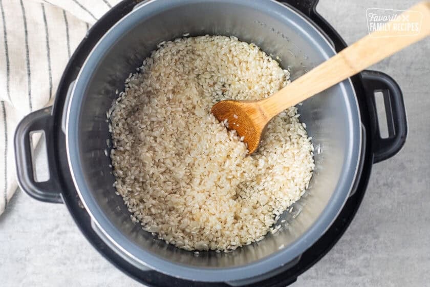 Instant pot with rice and white wine added and stirred with wooden spoon.