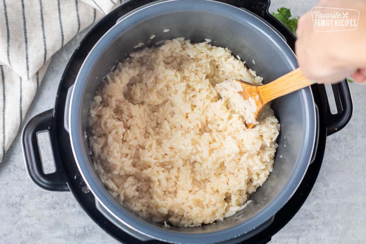 Stirring cooked risotto rice in an instant pot with a wooden spoon.