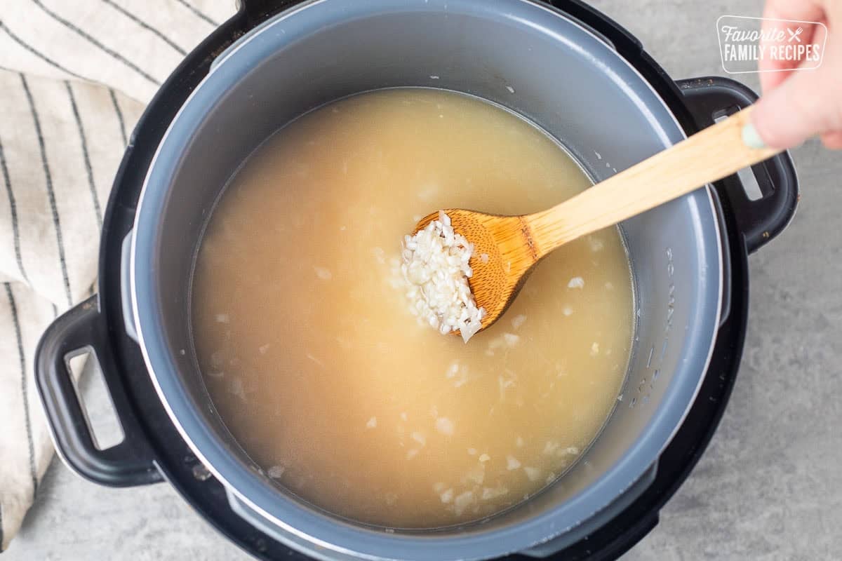 Using a wooden spoon, stirring chicken broth with rice in instant pot.