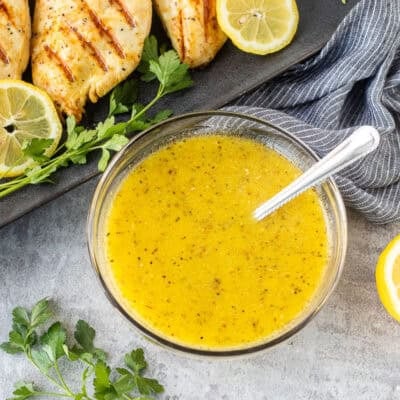 Bowl of lemon garlic chicken marinade with grilled chicken breasts on the side.