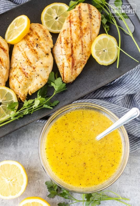 Bowl of lemon garlic chicken marinade with grilled chicken breasts on the side.