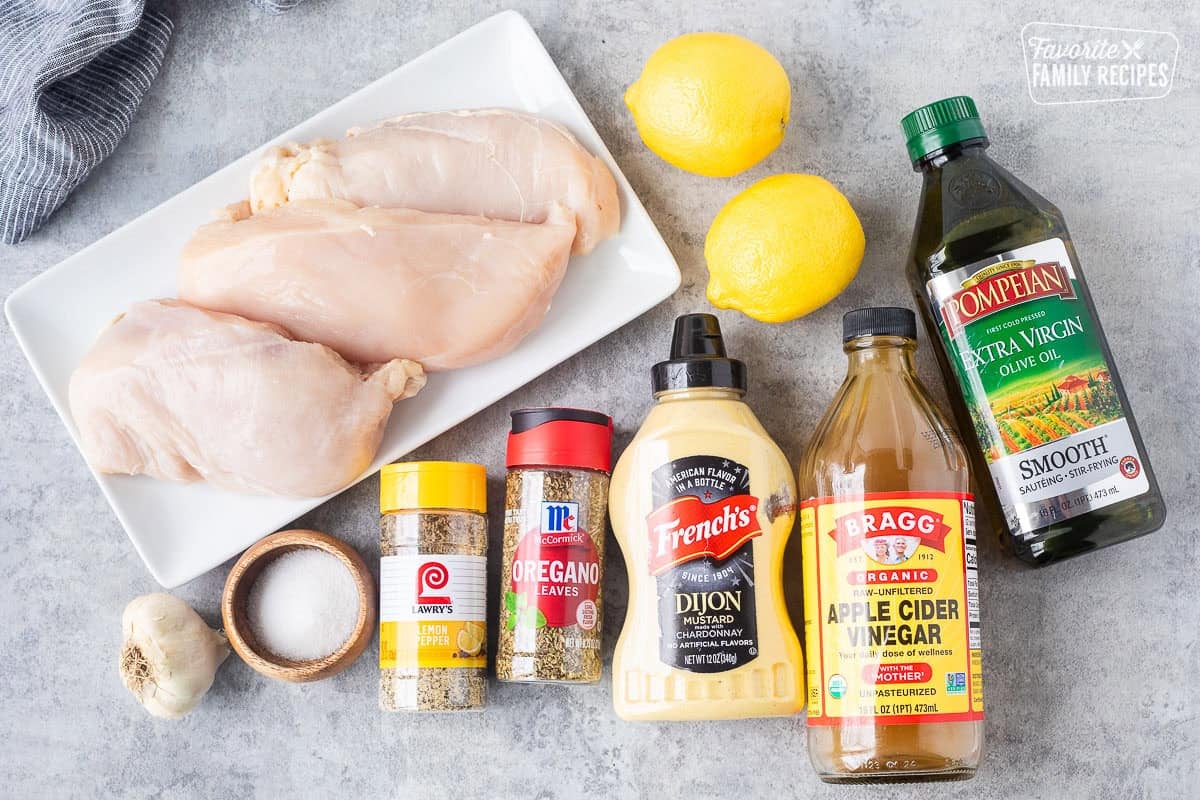Ingredients to make lemon garlic chicken marinade including olive oil, apple cider vinegar, dijon mustard, oregano leaves, lemon pepper seasoning, salt, garlic, lemon and chicken breasts.