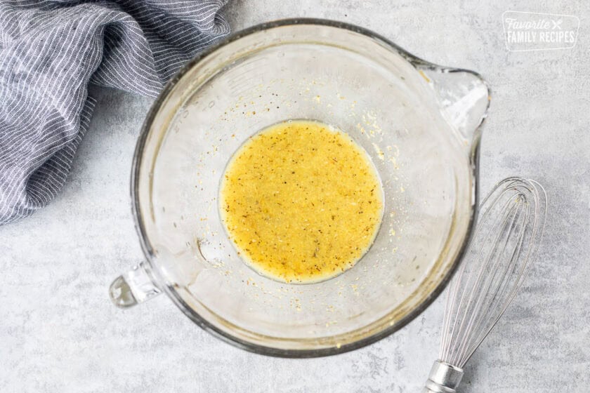 Glass bowl with lemon zest, juice and seasonings mixed. Whisk on the side.
